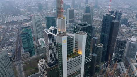 Pull-back-shot-of-top-part-of-Commerzbank-Tower.-tilt-up-reveal-downtown-skyscrapers-and-hazy-view-of-cityscape.-Frankfurt-am-Main,-Germany