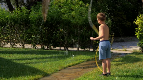 child having fun when watering lawn with hose