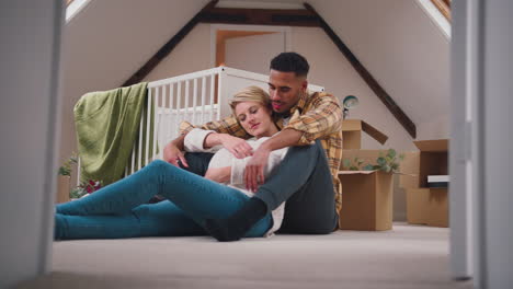 loving couple expecting baby hugging in nursery of new home together with moving in boxes