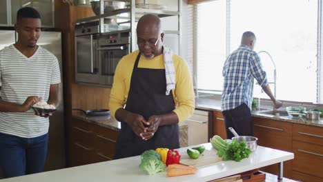 african american senior father and two adult sons standing in kitchen cooking dinner and talking