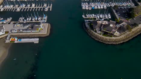 aerial tilt up reveals entrance to crowded boat harbor docks and blue sky