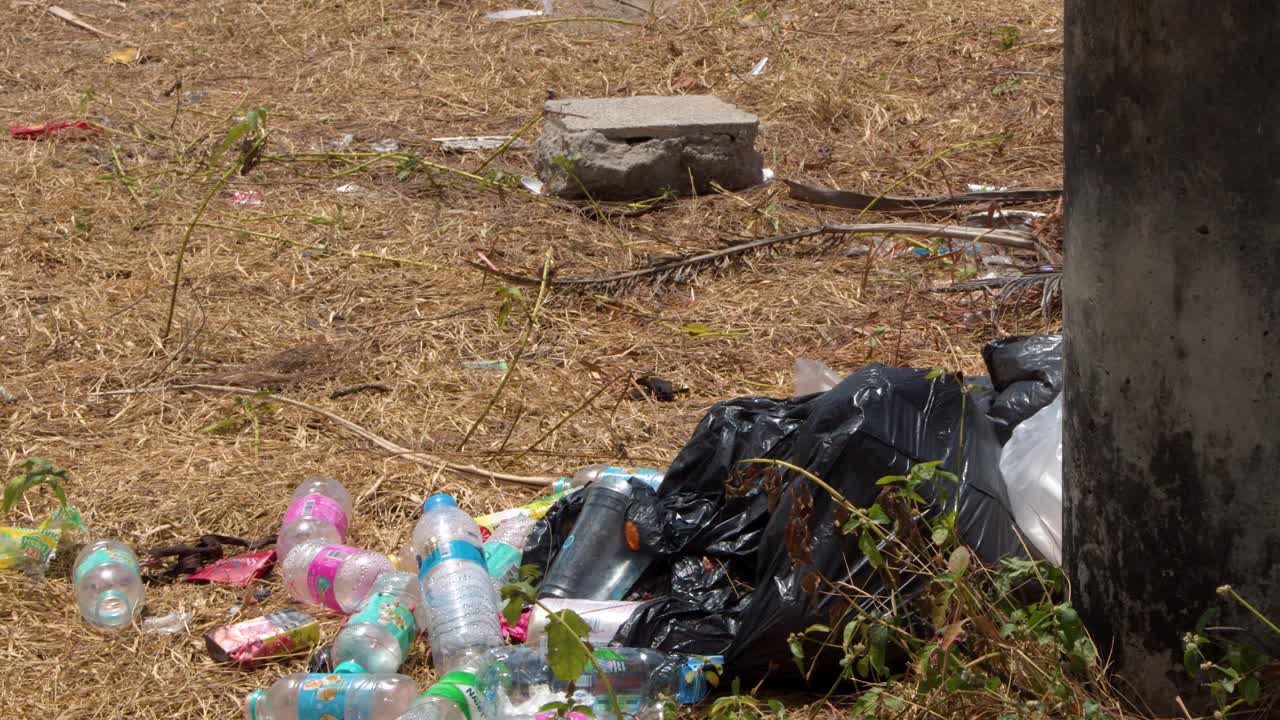 Una lenta panoramica della telecamera rivela bottiglie di plastica scartate e sacchi della spazzatura neri sull'erba secca.