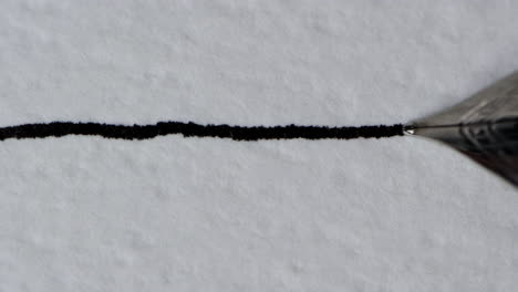 closeup of a fountain pen drawing a straight ink line on a textured paper surface