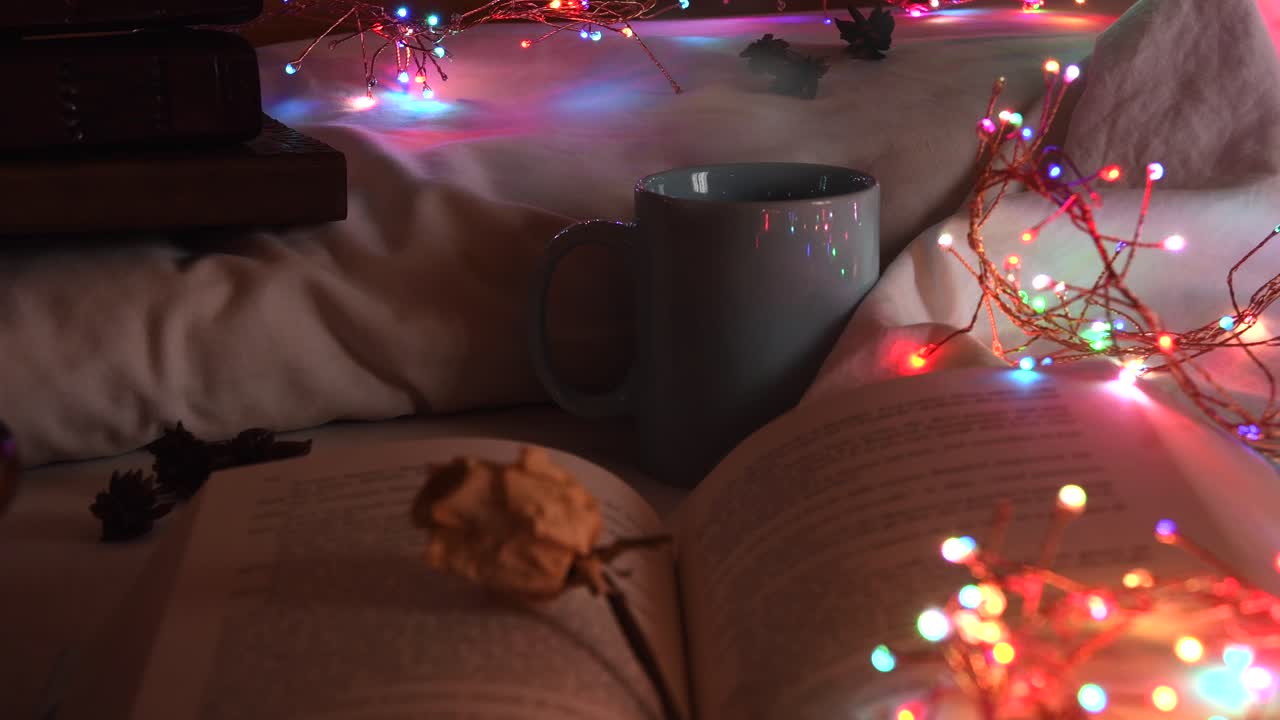 fondo acogedor de un libro abierto en una cama, al lado de una taza y rodeado de coloridas luces navideñas