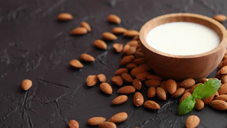 fresh almond milk in wooden bowl and almonds on black stone background