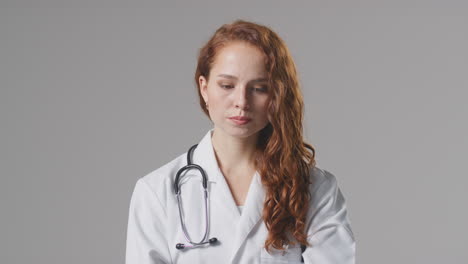 studio portrait of stressed female doctor with stethoscope in white coat against plain background