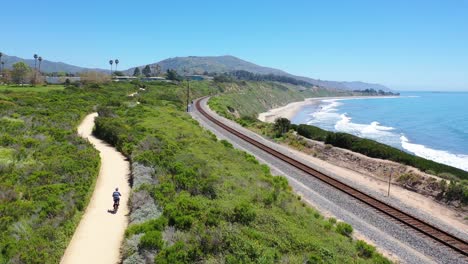 Antenne-Eines-Mannes,-Der-Sein-Fahrrad-Mit-Den-Bergen-Von-Santa-Barbara-Im-Hintergrund-In-Der-Nähe-Von-Carpinteria-California-2-Fährt