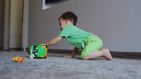 pretty little boy plays with his toy on the carpet. baby pushes the train and watches it ride. low angle view.