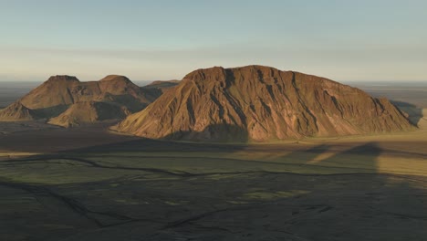 aerial view of sunlit mountains in thakgil, iceland, casting long shadows over the expansive plains, showcasing rugged and dramatic terrain.