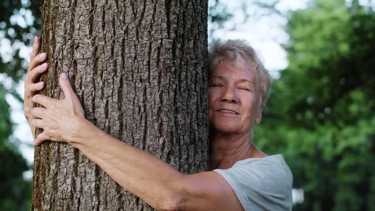 Cheerful senior woman embracing tree in the park.