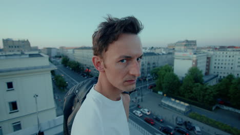 young man on city rooftop turns toward camera with serious expression