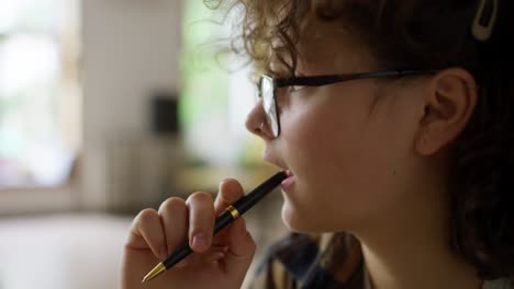 A-pensive-brunette-girl-with-curly-hair-and-glasses-takes-notes-while-she-studies-and-does-homework-in-the-university-library