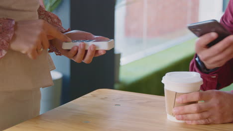 Close-Up-Of-Man-Making-Contactless-Purchase-In-Coffee-Shop-Using-Mobile-Phone