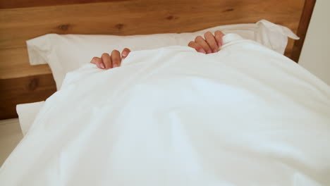 woman in bed wearing blue pajamas smiling joyfully at home in morning