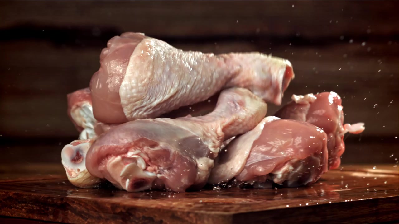 Fusi di pollo crudi che cadono e schizzano su un tagliere di legno