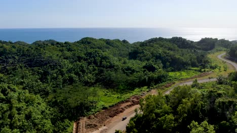 Dig-site-of-new-road-under-construction-in-vibrant-forest-area-of-Indonesia,-aerial-view