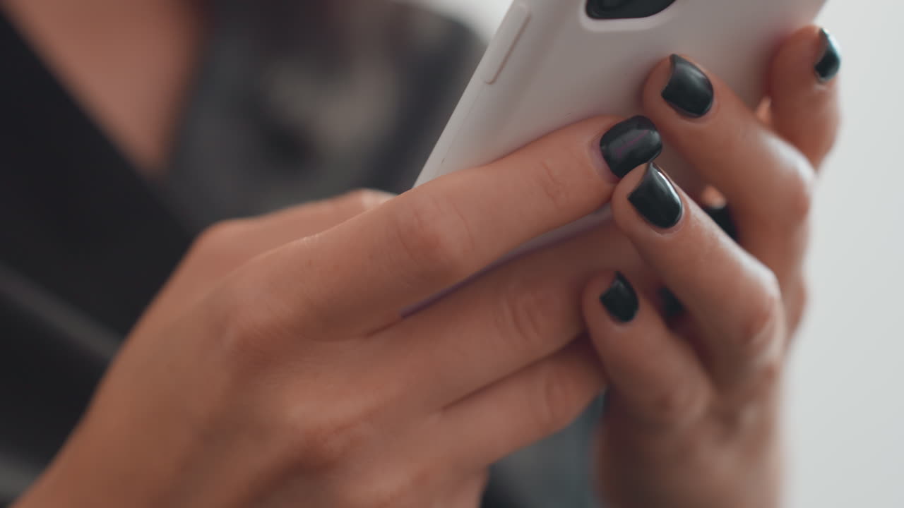 Hispanisk kvindehænder holder smartphone og skriver sms med mørk neglelak, nærbillede med lav dybdeskarphed, blødt naturligt lys, sløret baggrund, fokuseret gestus, influencer- og entrepreneur-vibes