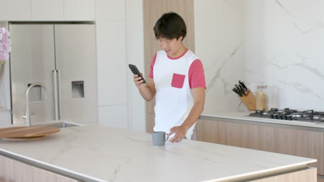 teenage asian boy checks his phone in a modern kitchen