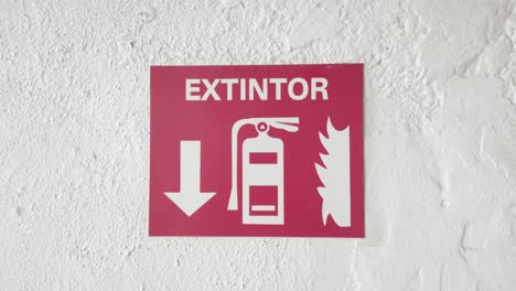 Red fire extinguisher sign on white wall, showing location with arrow pointing down
