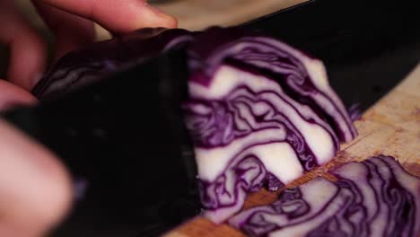 caucasian hands cuts a red cabbage in small pieces on wooden chopping board