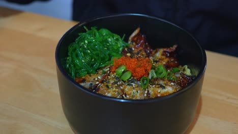 close-up of a person eating unagi don with seaweed and roe