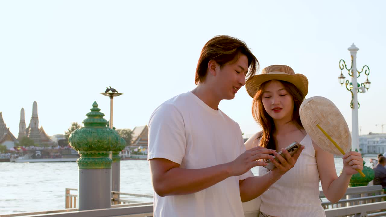 Pasangan tersenyum menggunakan smartphone di tepi sungai, berbagi peta, pencahayaan golden hour, suasana liburan santai