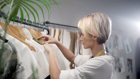 Woman-Tailor-Choosing-Clothes-In-The-Sewing-Workshop-And-Looks-At-Camera