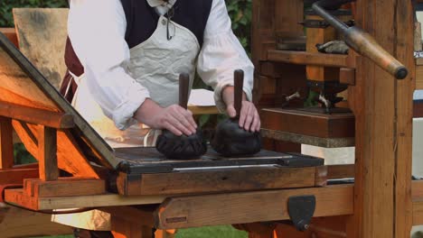 a revolutionary war re-enactor applies ink to the metal plates of an old 1700s printing press