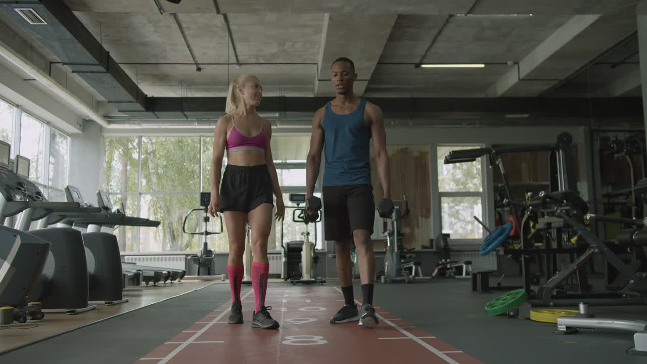 Caucasian female monitor and an athletic african american man in the gym.