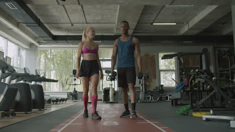 caucasian female monitor and an athletic african american man in the gym.