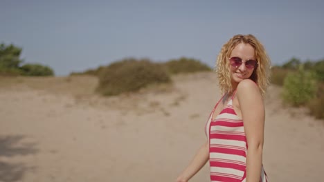 a joyful woman spins and laughs while standing in sunny sand dunes on a beautiful summer day