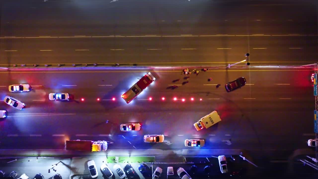 Pedestrian accident blocking lanes at night with emergency vehicles flashing lights and shutting down scene, drone top down