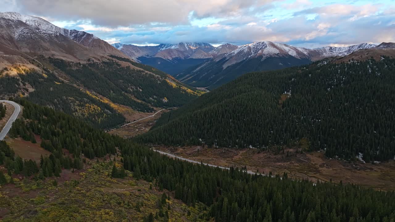 Drone view flying along a mountain highway framed by snow-capped peaks and expansive vistas in Colorado