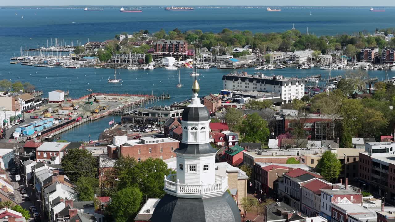 Cupola della State House di Annapolis Maryland con edifici storici del centro, porto turistico e barche sullo sfondo sotto la luminosa luce solare primaverile nella pittoresca città costiera degli USA. Ripresa aerea in lento avvicinamento