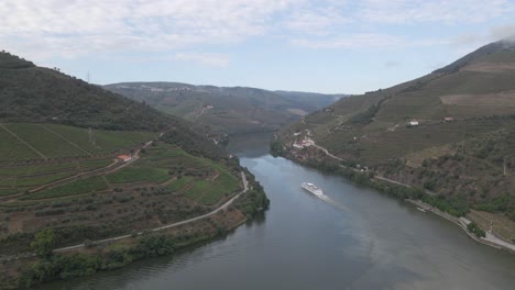 Vista-Aérea-De-La-Ciudad-Vinícola-De-Pinhão-Portugal,-Drone-Moviéndose-Hacia-La-Derecha-Sobre-El-Río-Duero-Mostrando-Las-Plantaciones-De-Vides-Y-Un-Barco-Turístico-Bajando-Por-El-Río.