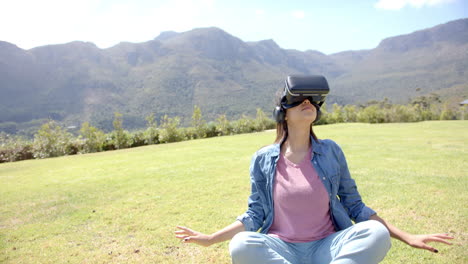 a young woman wearing virtual reality headset sits cross-legged outdoors