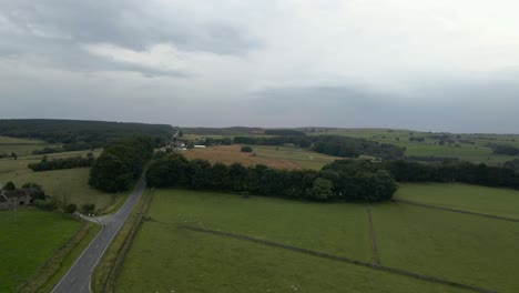 Eine-4K-Drohnenaufnahme,-Die-über-Die-Ringinlow-Road-Im-Peak-District-In-Der-Nähe-Von-Sheffield-Fliegt.-Der-Himmel-Ist-Bewölkt-Und-Grüne-Felder-Liegen-Auf-Der-Nebenseite-Einer-Langen,-Geraden-Straße