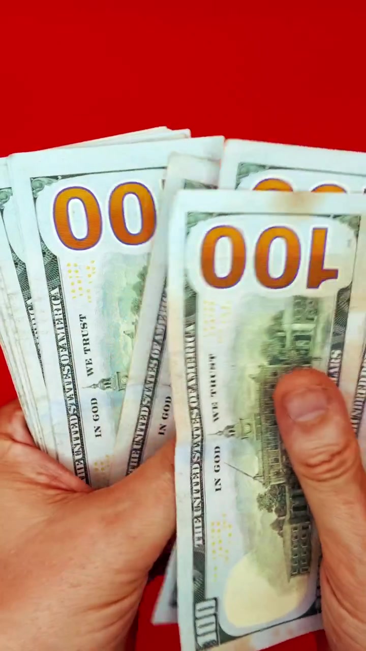 B-roll verticale 9:16: mani che sventagliano banconote da 100 dollari su sfondo rosso. Concetto per denaro veloce, motivazione alla ricchezza, transazione illegale, pagamento di stipendio, affari sul dark web e successo finanziario.