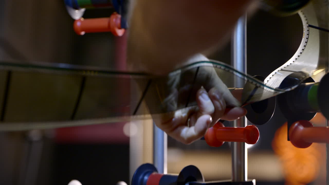 Medium shot of hands threading 70mm IMAX film through rollers