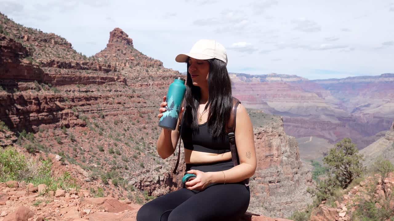 Giovane donna che beve acqua da una bottiglia mentre si riposa nel Grand Canyon