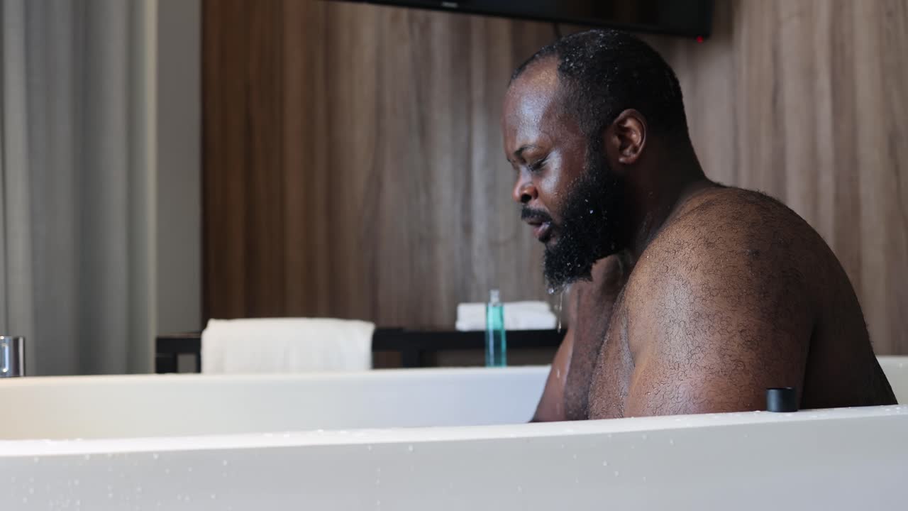 African American man is bathing in a bathtub in his hotel room while the window light touches his skin