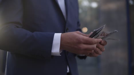 unrecognizable businessman on the street holding bundle of american money in his hands, counting it. wealthy male counts hundred