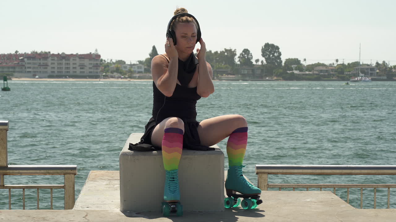 Attractive adult woman wearing rollerskates while listening to music in headphones with pacific ocean in background