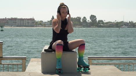 attractive adult woman wearing rollerskates while listening to music in headphones with pacific ocean in background