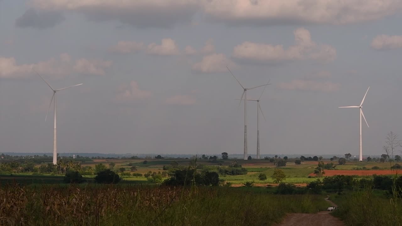 Wind Turbines Towering Farmlands, as farmers grow their crops and tend their animals; clean alternative energy in Thailand and mainland Southeast Asia.