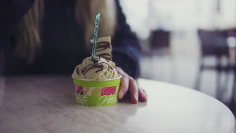 close up of a blond haired girl eating an artisan ice cream with a spoon outside of a cafe