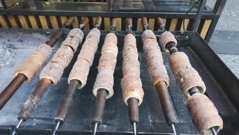 close-up of traditional czech trdelník pastries baking on rotating spits over an open flame, showcasing their golden, sugar-coated exterior