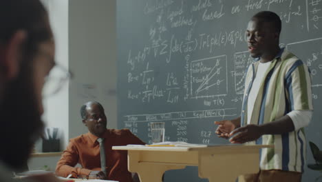 man giving a scientific presentation in front of a chalkboard