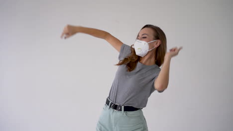 Young-cheerful-woman-dancing-and-wearing-medical-face-mask-on-white-background.-End-of-the-coronavirus-quarantine.
