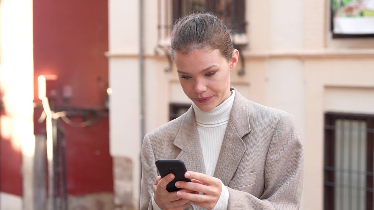 A joyful young woman is happily smiling while using her smartphone in a vibrant urban setting